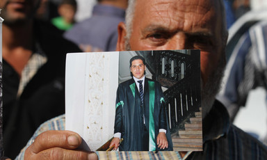 Older man holds photograph of young man wearing graduation gown