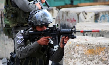 An Israeli Border Police officer aims a rifle from behind a concrete block
