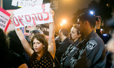 A pair of Israeli police officers, one a woman and the other a man, watch as a protesting woman holds a Hebrew-language sign over her head