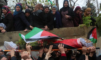 Mourning women look down on youth's body as he is carried in funeral procession