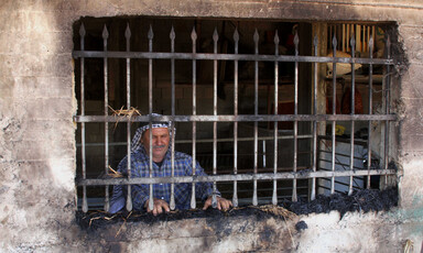 Man stands behind barred window in burned-out room