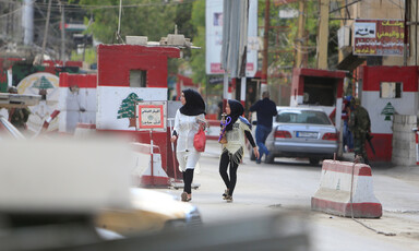 A woman and girl walk in front of car at checkpoint painted with colors and emblem of Lebanese flag