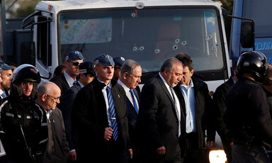 Group of men walk in front of truck with bullet holes in windshield