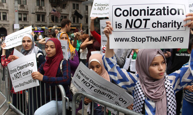 Young women hold up signs reading: Colonization is NOT charity www.stoptheJNF.org