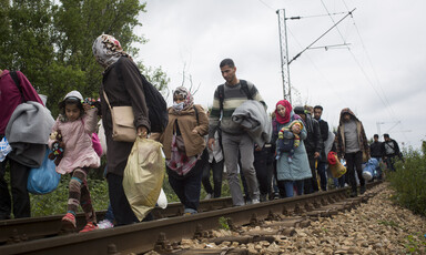 Men, women and children walk along railroad tracks while carrying their possessions