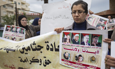 A woman holds a banner and a poster showing photos of slain men whose bodies are being held by Israel