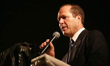 Close-up of Nir Barkat standing at a podium while holding a microphone to his mouth