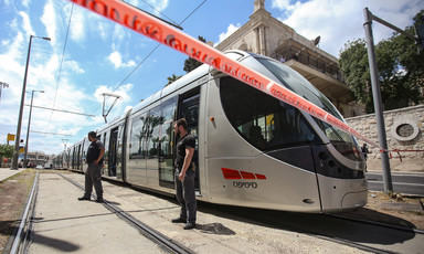 Two guards stand in front of light rail train surrounded by red tape