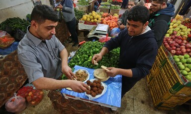 Two men stand at table making falafel sandwiches in middle of produce shop