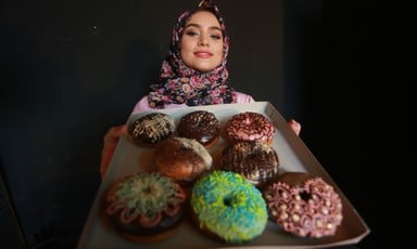 Young woman holds up a tray of doughnuts with varying toppings