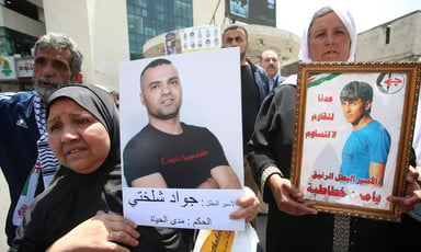 Women hold posters showing photos of men detained by Israel