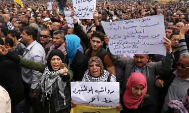 Men and women hold Arabic-language signs protesting salary cuts during large demonstration