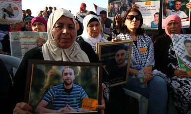 Women sitting on chairs hold photos of men being detained by Israel