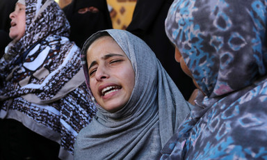 Girl wearing head scarf, seen from shoulders up, is comforted by woman while she cries