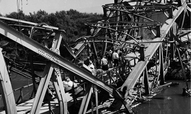 Black and white photo shows people walking across badly damaged bridge