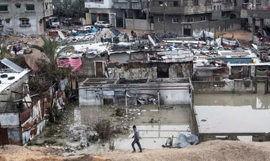 Wide view of boy walking in front of flooded neighborhood of shanty dwellings