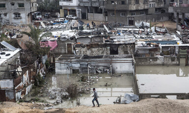 Wide view of boy walking in front of flooded neighborhood of shanty dwellings