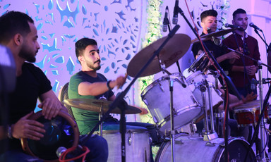 Close-up on young man playing on a drum kit with a tabla player and two singers standing on either side of him
