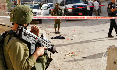 An Israeli soldier holding a rifle stands guard at a site marked by police tape