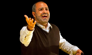 Close-up of actor viewed from waist up gesturing up with his hand as he speaks