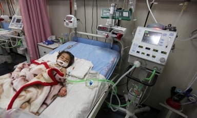 A toddler lies on a hospital bed hooked up to several medical machines and an IV drip.