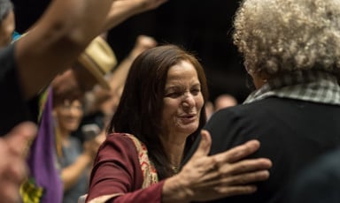 Rasmea Odeh, seen from chest up, puts a hand on the back of Angela Davis, seen from the back