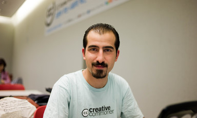 Smiling young man with goatee wearing Creative Commons t-shirt is seen from chest up