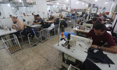 Photo shows men working at sewing machines in garment factory