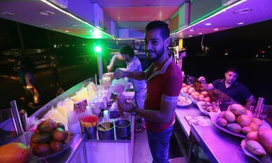 Smiling young man pours smoothie mix into a plastic cup at an outdoor juice stand