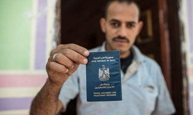Man holds up passport-style document that says Arab Republic of Egypt Travel Document for Palestinian Refugees
