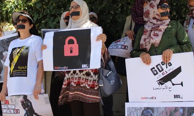 Photo of women with their mouths covered holding campaign signs condemning G4S and expressing solidarity to Palestinian hunger strikers. 