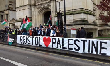 Long banner reading Bristol <3 Palestine is displayed by a crowd  waving Palestine flags outside a campus building