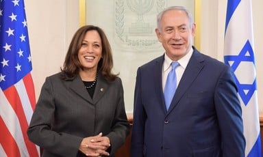 Smiling Kamala Harris stands next to Benjamin Netanyahu, also smiling, as the pair are flanked by American and Israeli flags