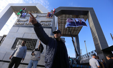 A Palestinian Authority officer raises an arm with a pointed index finger as he stands in front of Rafah crossing, decorated with posters of Mahmoud Abbas and Abdulfattah al-Sisi