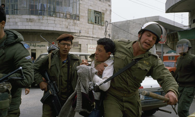 Photo shows an Israeli soldier with his arm around the neck of a Palestinian youth as other soldiers look on