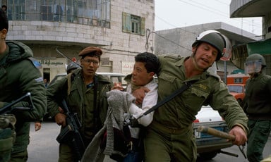 Photo shows an Israeli soldier with his arm around the neck of a Palestinian youth as other soldiers look on