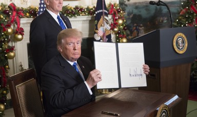 Trump sits at desk holding up newly signed executive order as Vice President Pence stands behind him