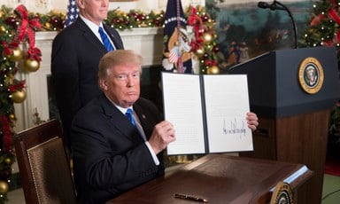 Trump sits at desk holding up newly signed executive order as Vice President Pence stands behind him