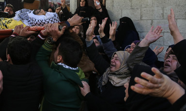 Photo shows crying women waving their hands at shrouded body of young man being carried on stretcher
