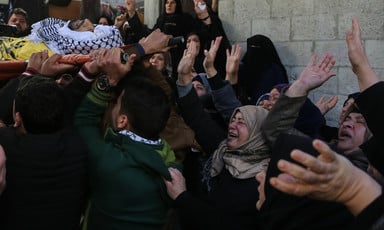 Photo shows crying women waving their hands at shrouded body of young man being carried on stretcher