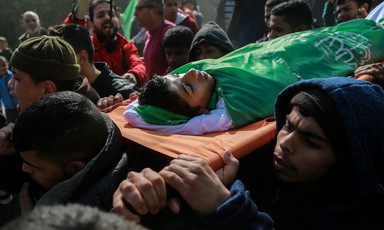 Shrouded body of boy is carried on a stretcher during funeral procession