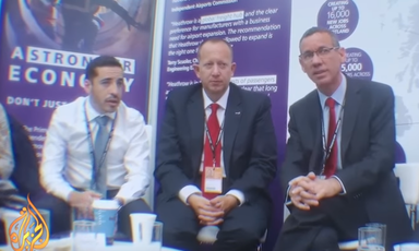 Three men with conference lanyards sit next to each other in a similar pose.