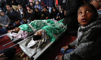 The shrouded bodies of two boys, wrapped in green flags, lay on stretchers while surrounded by mourners
