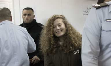 Ahed Tamimi, wearing prison uniform, smiles while surrounded by police