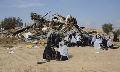 Several women sit in front of pile of debris 