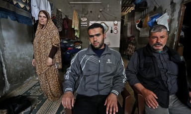 Father and son sit in chairs as mother stands behind them next to clothing line