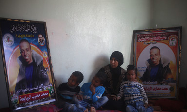 Woman and three small children sit on floor next to two large posters of smiling young man