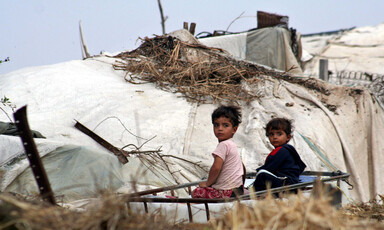 Photo shows small children sitting in front of tent shelter