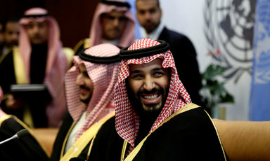 Saudi crown prince is seen smiling from chest up while wearing robe and checkered headdress