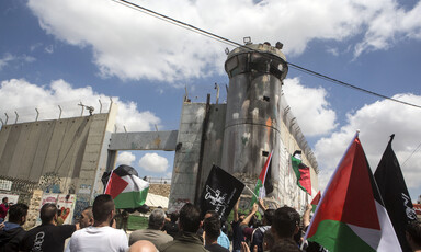 Dozens of protesters carrying Palestinian flags near the apartheid wall.